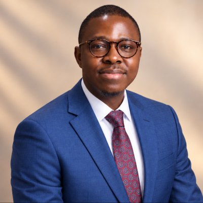 Portrait of Ezekiel Ologunde in a blue suit and burgundy tie against a warm peach backdrop.